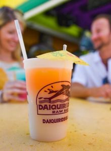 A daiquiri with an umbrella on a table, with two people blurred in the background, suggesting a relaxed, tropical setting.